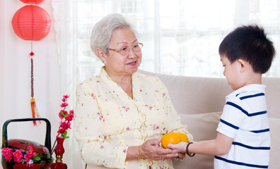 Asian boy giving mandarin oranges to his grandmother