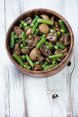 Wooden bowl with roasted champignons, peas and beans, above view