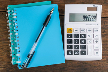 Calculator with notebook & pen on wooden background