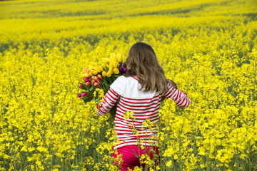 Child walking in a field of rapeseed with Spring flowers