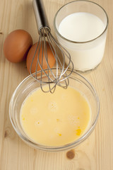 Beat eggs with milk in a glass bowl ,   eggs on a wooden table.