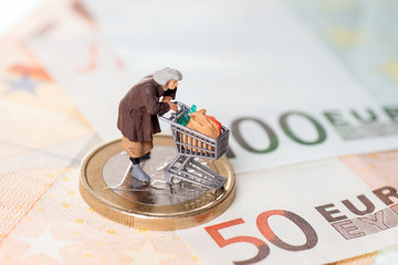 Alte Frau mit Einkaufswagen auf einem Geldstück mit Banknoten