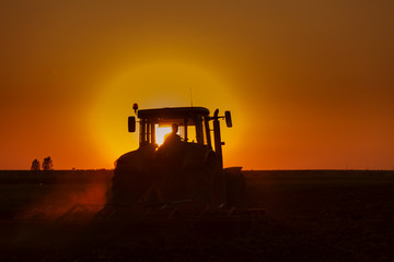 Tractor Plowing in dusk on sunset with crows