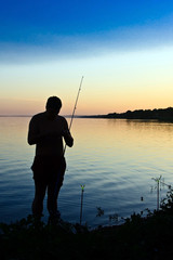 Fisherman with fishing rod standing close to lake