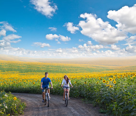 Fototapeta premium Teen couple riding bike in sunflower field