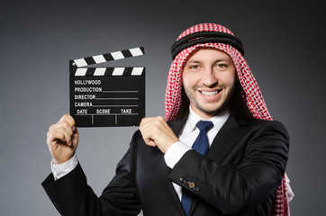 Arab man with movie clapper against grey background