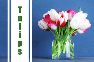 Beautiful tulips in glass jug on color wooden background