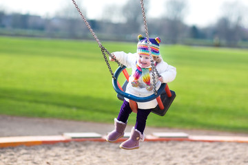 Happy laughing toddler girl swinging on a playground