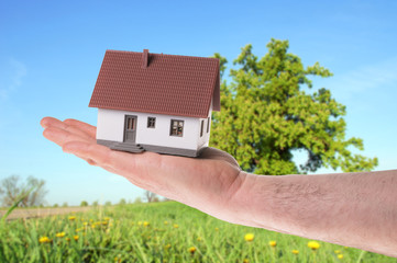 Hand hält ein kleines Haus in der Natur