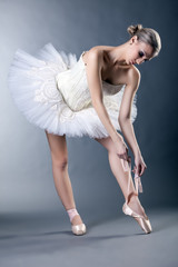 Beautiful young ballerina tying pointe in studio