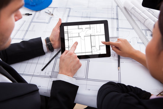 Architects With Digital Tablet Working On Blueprint