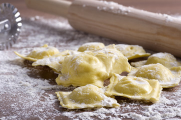 homemade uncooked ravioli with a roller on wooden table