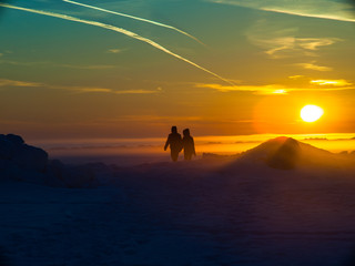 Two people are on the snow on sunset background