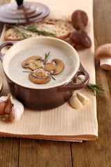 Mushroom soup in pot, on wooden background