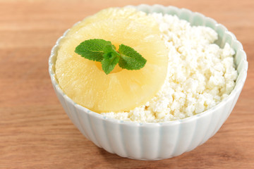 Bowl of tasty cottage cheese with pineapple on wooden table