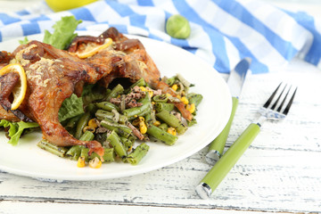 Roasted quails with vegetables on plate, on wooden background