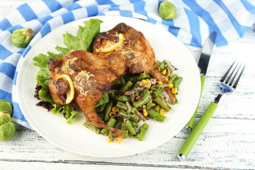 Roasted quails with vegetables on plate, on wooden background