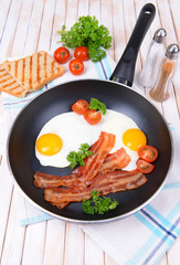 Scrambled eggs and bacon on frying pan on table close-up