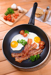 Scrambled eggs and bacon on frying pan on table close-up
