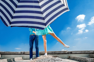 Couple hiding under the beach umbrella on the roof on blue sky b