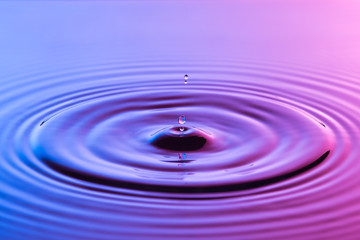 Water drop close up with concentric ripples colourful blue and p