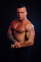 Fototapeta premium Handsome muscular man poses and shows biceps on dark background