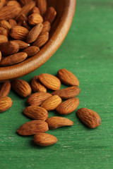 Almonds in bowl on color wooden background