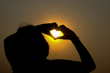 hands forming a heart shape in the sunset