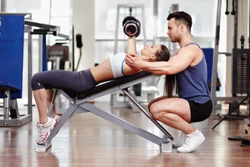 Tuinposter Personal trainer helping woman at gym © Xalanx