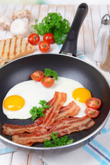 Scrambled eggs and bacon on frying pan on table close-up