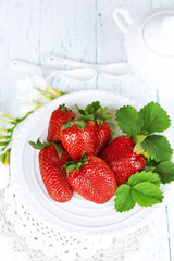 Strawberries with leaves on plate, on wooden background