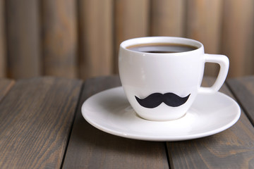 Cup with mustache on table on wooden background