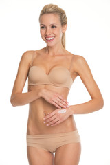 Obraz premium Smiling young woman in lingerie applying creme on hand