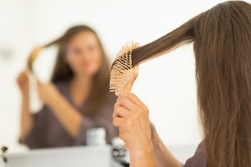 Young woman combing hair in bathroom. rear view