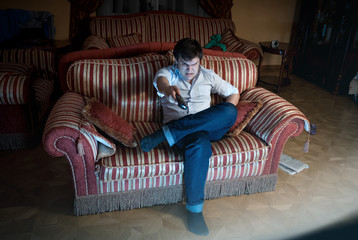 Obraz premium angry man switching TV channel while sitting on sofa