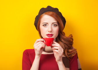 Redhead girl with red cup of coffee or tea on yellow background.