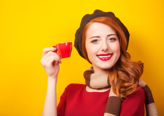 Redhead girl with red cup of coffee or tea on yellow background.