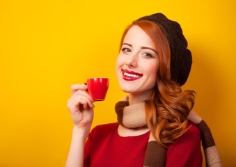Redhead girl with red cup of coffee or tea on yellow background.