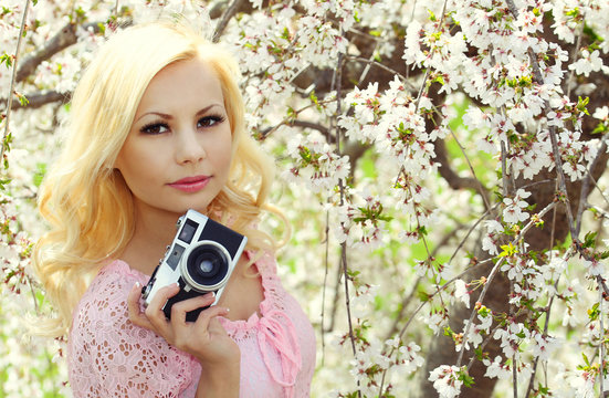 Blonde Girl with Retro Camera over Cherry Blossom. Beautiful