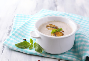 Mushroom soup in white pot, on napkin,  on wooden background