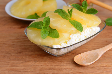 Bowl of tasty cottage cheese with pineapple on wooden table