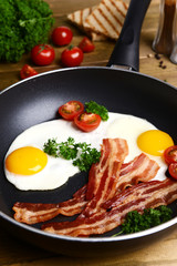 Scrambled eggs and bacon on frying pan on table close-up