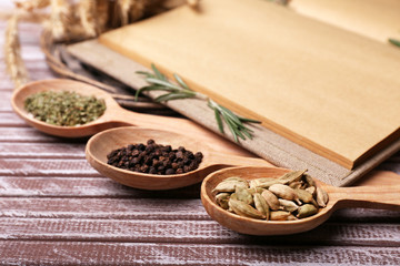 Different spices and cook book on wooden table, close up