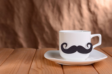 Cup with mustache on table on brown background