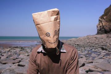 Man with paperbag over his head on the beach - obrazy, fototapety, plakaty