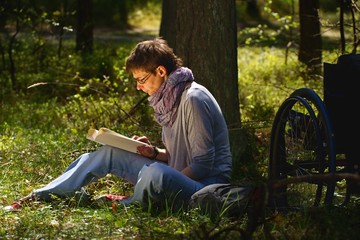 Disabled woman reading a book in the forest, wheelchair