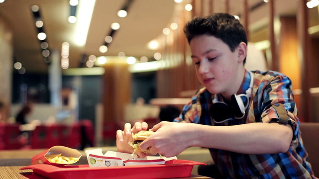 Young teenager eating tasty hamburger in fast food restaurant