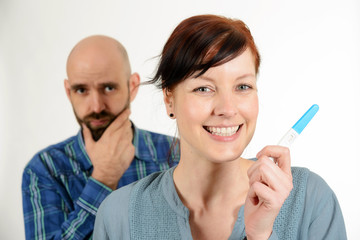 Unsicherer Mann und lachende Frau mit Schwangerschaftstest