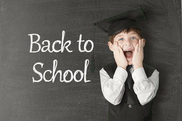 Cheerful little boy on blackboard. Looking at camera