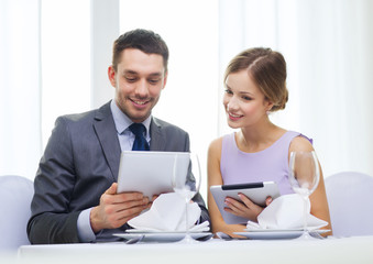 couple with menus on tablet pc at restaurant